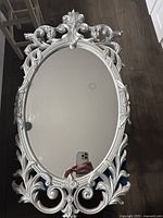 Full view of silver ornate oval mirror on floor