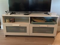 Front view of white TV stand showing open shelves, drawers with frosted glass fronts, and overall appearance