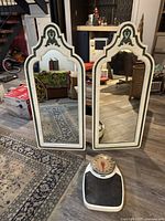 Two vintage wooden wall mirrors with white and green wood frames leaning against the wall, placed next to a vintage metal scale with a black platform and circular dial.