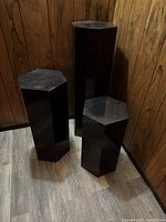 Three black acrylic hexagonal pedestals arranged together in a corner showing height variation and overall condition including surface scratches and smudges.