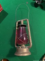 Side view of vintage brass oil lamp with red glass chimney on a green surface.