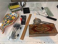 Full overview of lot including ceramic fish dish, wooden box, various bar tools, ruler, CDs and other small items on white table.