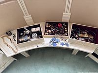 Overview of multiple boxes containing assorted costume jewelry including bracelets, earrings, necklaces, brooches, and pendants.