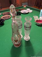 Leaded crystal decanter with cranberry accents and stopper alongside two tall crystal vases on green surface with other items visible in background.