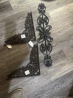 Three metal decorative wall panels laid on floor; two corner panels and one long floral panel.