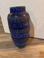 Blue floor vase with textured Fat Lava bands shown fully upright on wooden floor against white background.