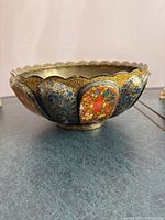 Side view of scalloped, hand-painted wooden bowl showing floral enamel patterns in red, blue, and gold.