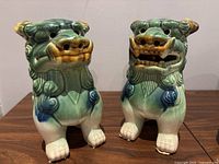Front view of both Foo Dogs showing their green glaze with blue and brown accents, seated poses, and detailed facial features.