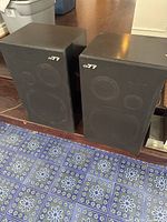Pair of black CX-77 vintage speakers side by side, showing front mesh grille, drivers, and logo with minor wear.