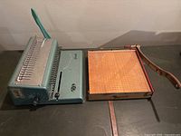 Full view of the metal binding machine and the wooden lever paper cutter placed side by side.