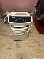 Front view of white Whirlpool dehumidifier showing air vents and top control panel with attached power cord.