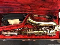 Polished brass saxophone laid inside red velvet-lined hard case along with accessories such as a mouthpiece and neck strap.