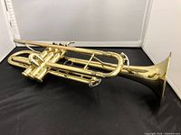Side view of the brass trumpet showing the entire instrument with its shiny polished brass finish and three valves.