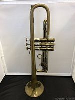 Side view of the brass trumpet showing the long, curved tubing and the bell with a small dent.