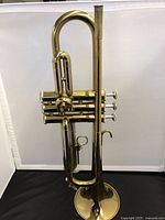 Front view of the brass trumpet standing upright showing the tubing and valves.