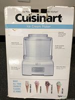 Front of the white and light blue Cuisinart Ice Cream Maker box showing the unit image and text describing features including heavy duty motor, advanced mixing paddle and double insulated freezer bowl. Box has noticeable damage.
