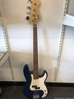 Full view of bass guitar front showing blue body, white pickguard, rosewood fingerboard with dots, and four strings.