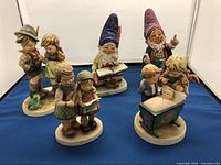 Overall group photograph of the 5 Goebel figurines on a blue cloth background, showing all figurines spaced separately