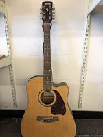 Full front view of the acoustic electric guitar showing natural wood body with cutaway, pickguard, neck, and headstock with Ibanez branding.