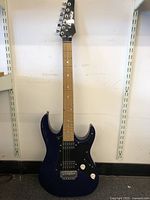 Full front view of blue Ibanez GIO electric guitar standing upright showing the entire body and neck.