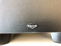 Close-up of Klipsch logo on black surface indicating part of the subwoofer or speaker.