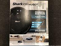 Front of box showing model Shark ION Robot with features: powerful suction, tri-brush system, deep cleaning on carpets and floors, pet hair pickup, color black.