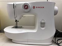 Front and side view of white Singer MX60 sewing machine showing stitch selector dial and machine body shape