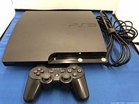 Black Sony PlayStation 3 gaming console and black DualShock 3 controller with power cord coiled beside console.