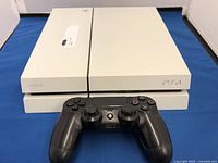 Top view of white Sony PlayStation 4 console with black wireless controller in front.