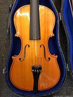 Top close-up view of the violin lying within its blue-lined black case, highlighting the body and chin rest.