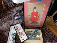 Image showing the full lot including three pieces of Asian style art: a large framed emperor portrait and two long framed floral tile paintings placed on carpeted floor.