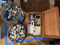 Two round metal containers and one wooden box filled with assorted buttons in various sizes and colors.