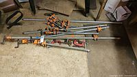 Mixed collection of bar clamps, pipe clamps, and C-clamps arranged on floor