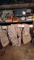 Three khaki fishing vests hanging on wire hangers in basement environment, showing condition and style.