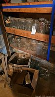 Wooden shelves with multiple clear glass Mason jars mostly quart and pint size, some in cardboard boxes below.