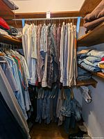 View of men's shirts and jeans hanging in closet showing variety of patterns and colors.