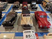 Front row of three model cars including black convertible, cream convertible with soft top, and red sedan, all detailed with chrome and realistic wheels.