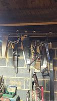 Hand tools hanging on a wall including multiple handsaws, clamps, and levels.