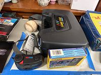 Sega Game Gear console box, baseball, Casio mini TV box and Vivitar EcoSun 777 film camera visible on surface