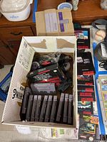 Top-down view of box containing loose SNES cartridges, two controllers, assorted cables, and Warlock game box