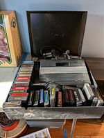Atari 7800 console with numerous game cartridges in black case displaying condition and assortment of games.