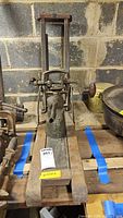Vintage hand drill with visible wooden base, crank handle, metal gears in basement setting.