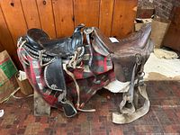Side view of two Western pony saddles on a wooden stand covered with a plaid blanket.