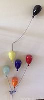 Full view of six colored glass balloons on metal wire frame mounted to wall