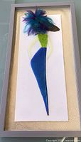 Blue-green fused glass female figure with feather plume hat in grey frame