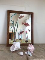 Full view of wood framed mirror with mosaic ocean scene and four shells in front