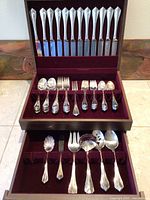 Flatware set displayed in open wooden chest showing knives, forks, spoons and serving pieces