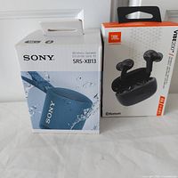 Photo displaying the sealed retail boxes of Sony SRS-XB13 wireless speaker and JBL Vibe 200TWS earbuds.