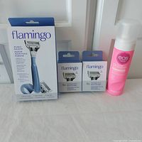 Front view of all items including Flamingo pubic razor in sealed box, two boxes of replacement cartridges, and EOS shea butter shave cream bottle.
