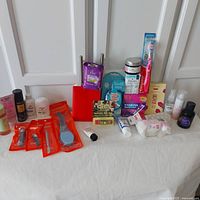 Photo of the full lot showing all items on a white surface in front of white doors, including travel accessories, beauty, skincare, haircare, and personal care products.